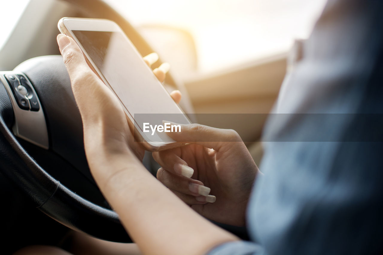 Cropped hands of woman using mobile phone in car