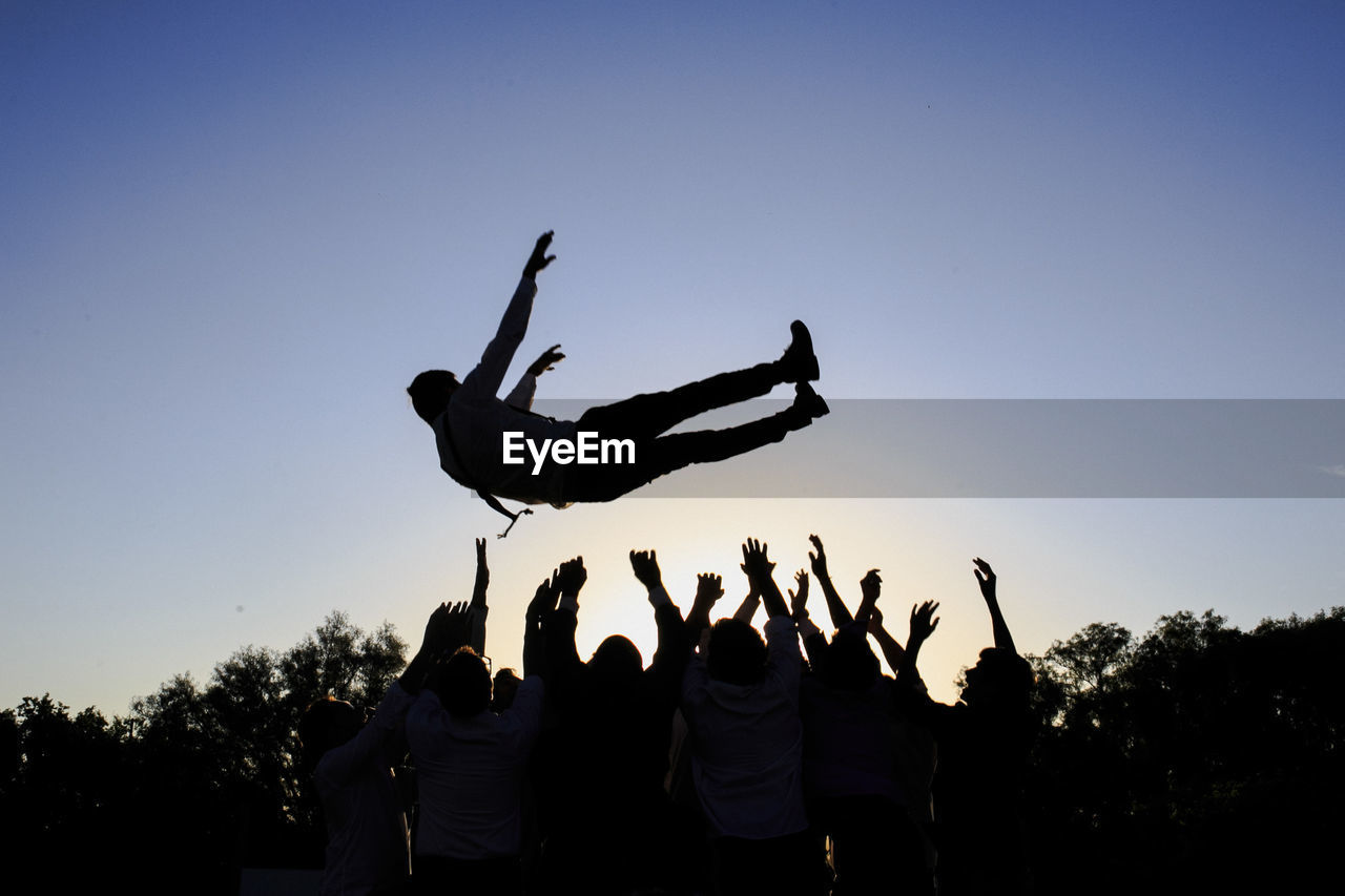 Man jumping over friends against clear sky