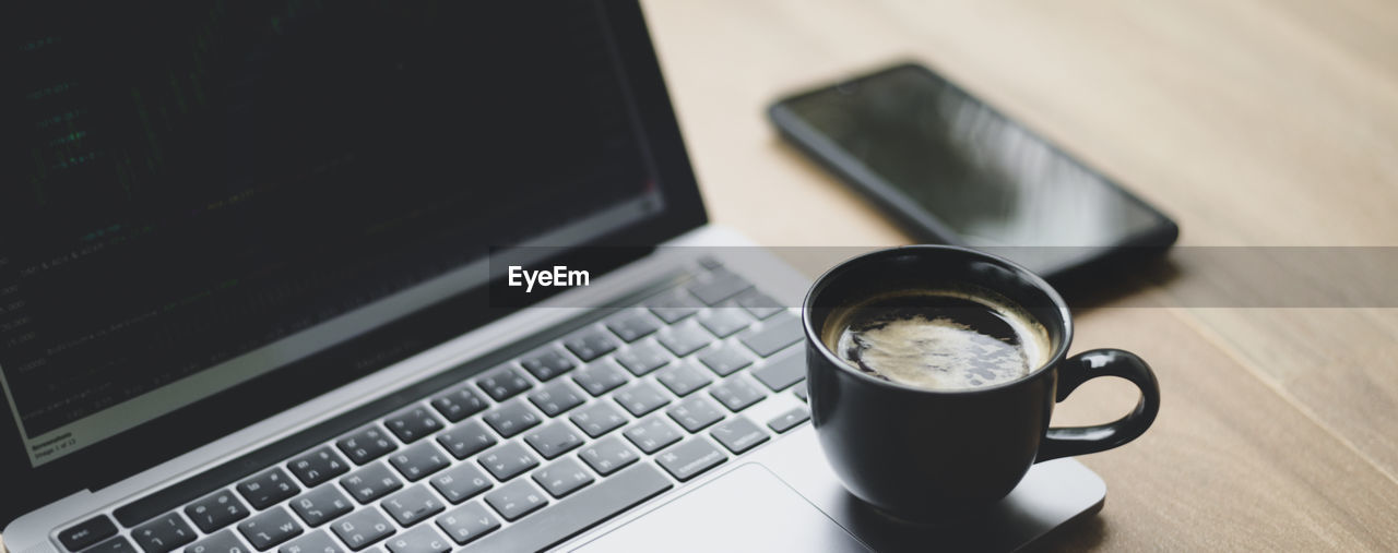 Coffee mug placed on laptop with stock chart on screen, close up shot.