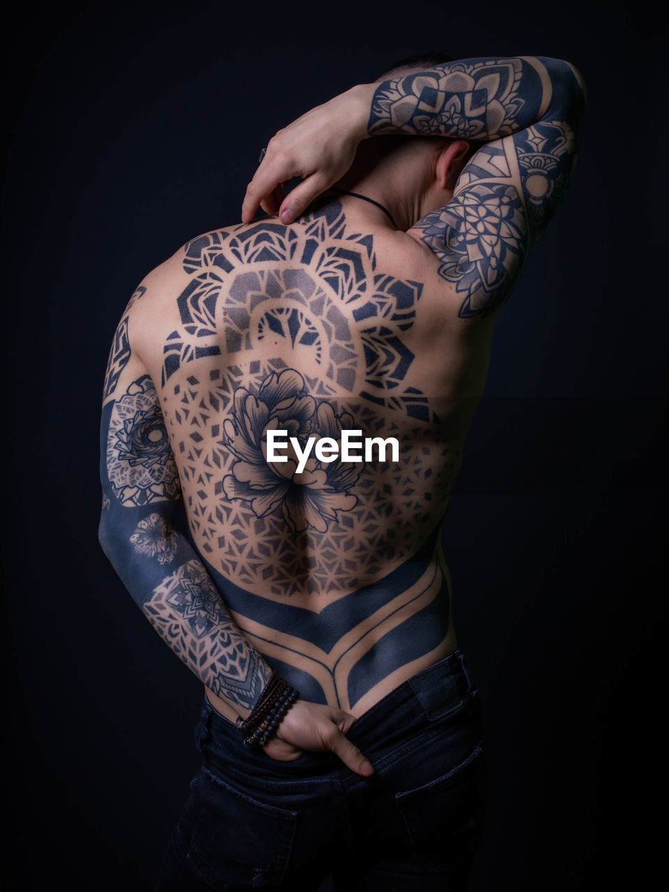 Rear view of shirtless man with tattoo standing against black background