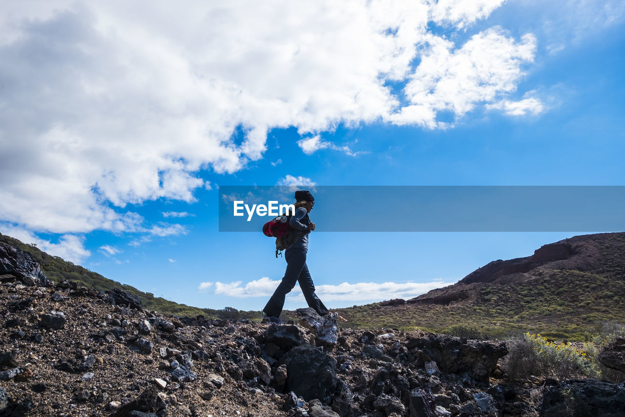 Side view of woman walking on rock against sky