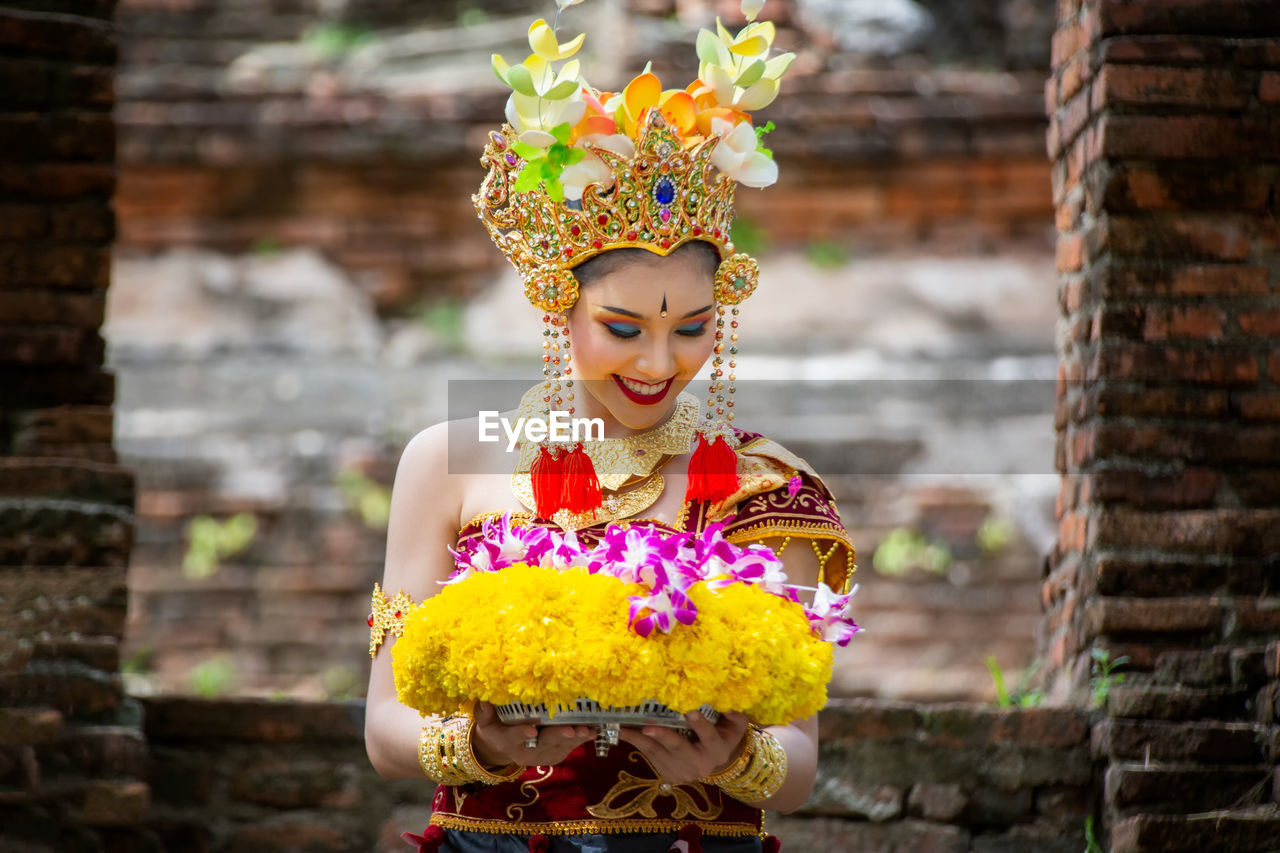 Smiling young woman in traditional clothing holding flowers at temple