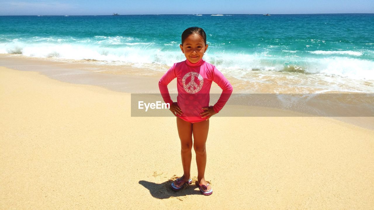 Full length portrait of girl standing on shore at beach during sunny day