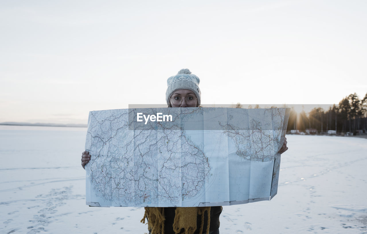 Woman holding up a large map whilst standing on a frozen lake