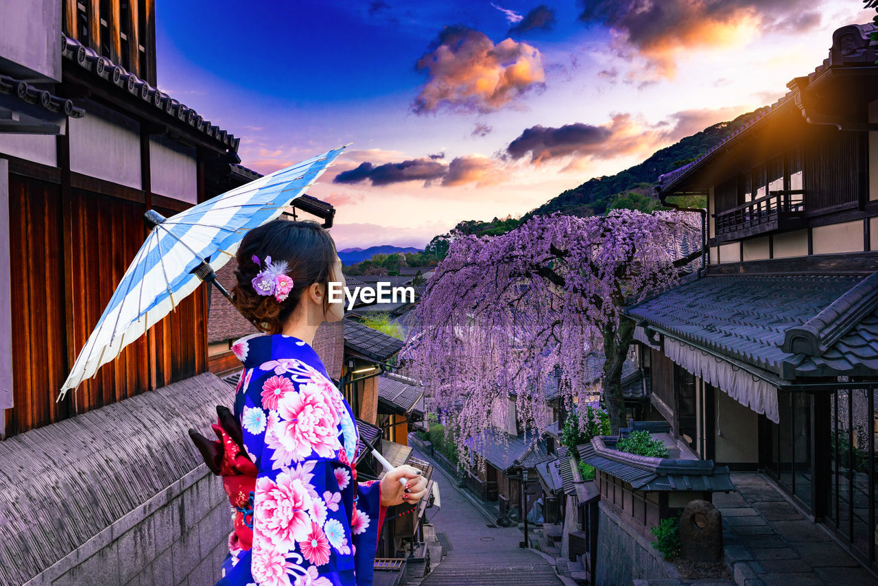 Woman in kimono standing in city during sunset