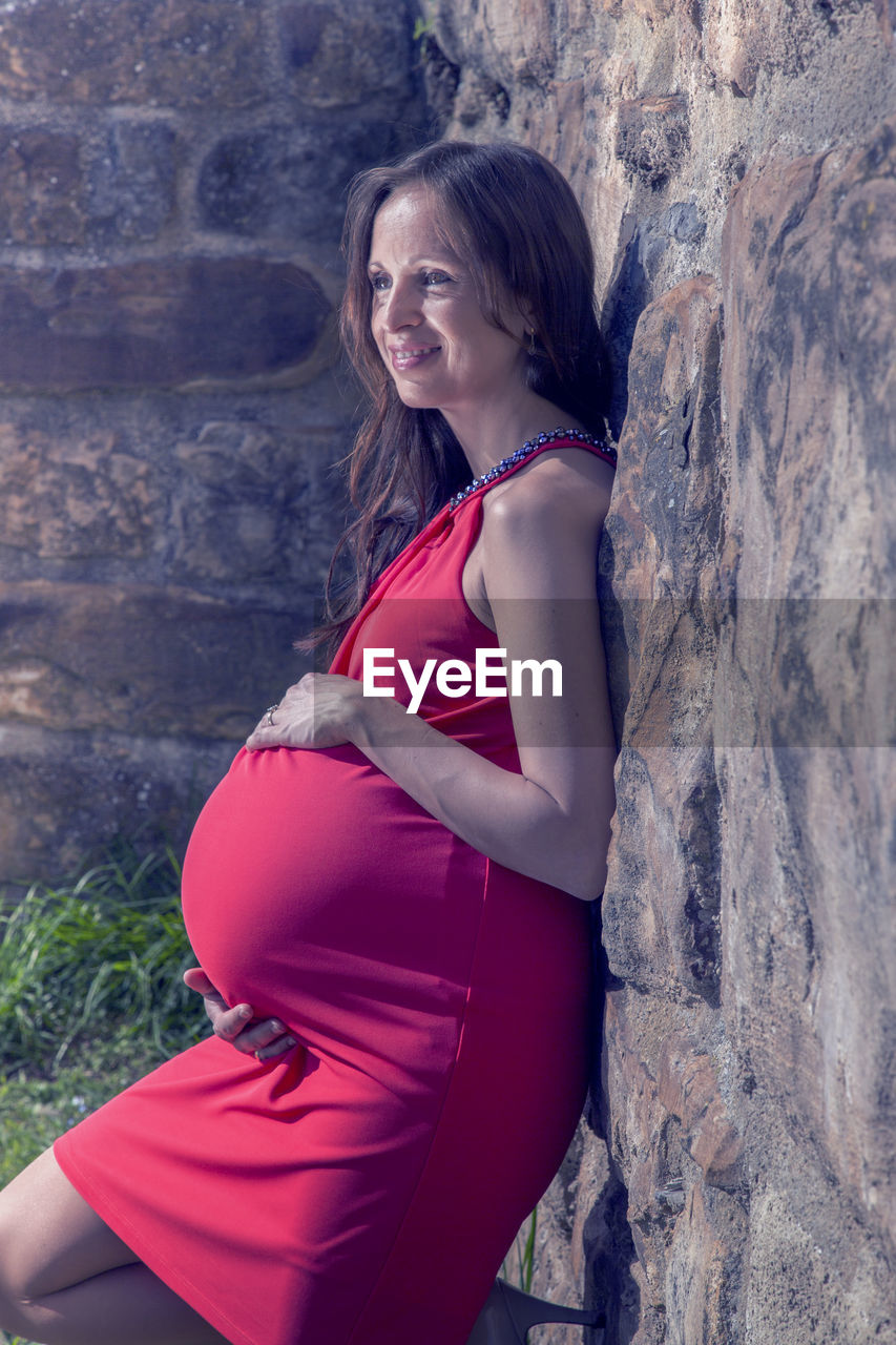 Side view of pregnant woman leaning on stone wall