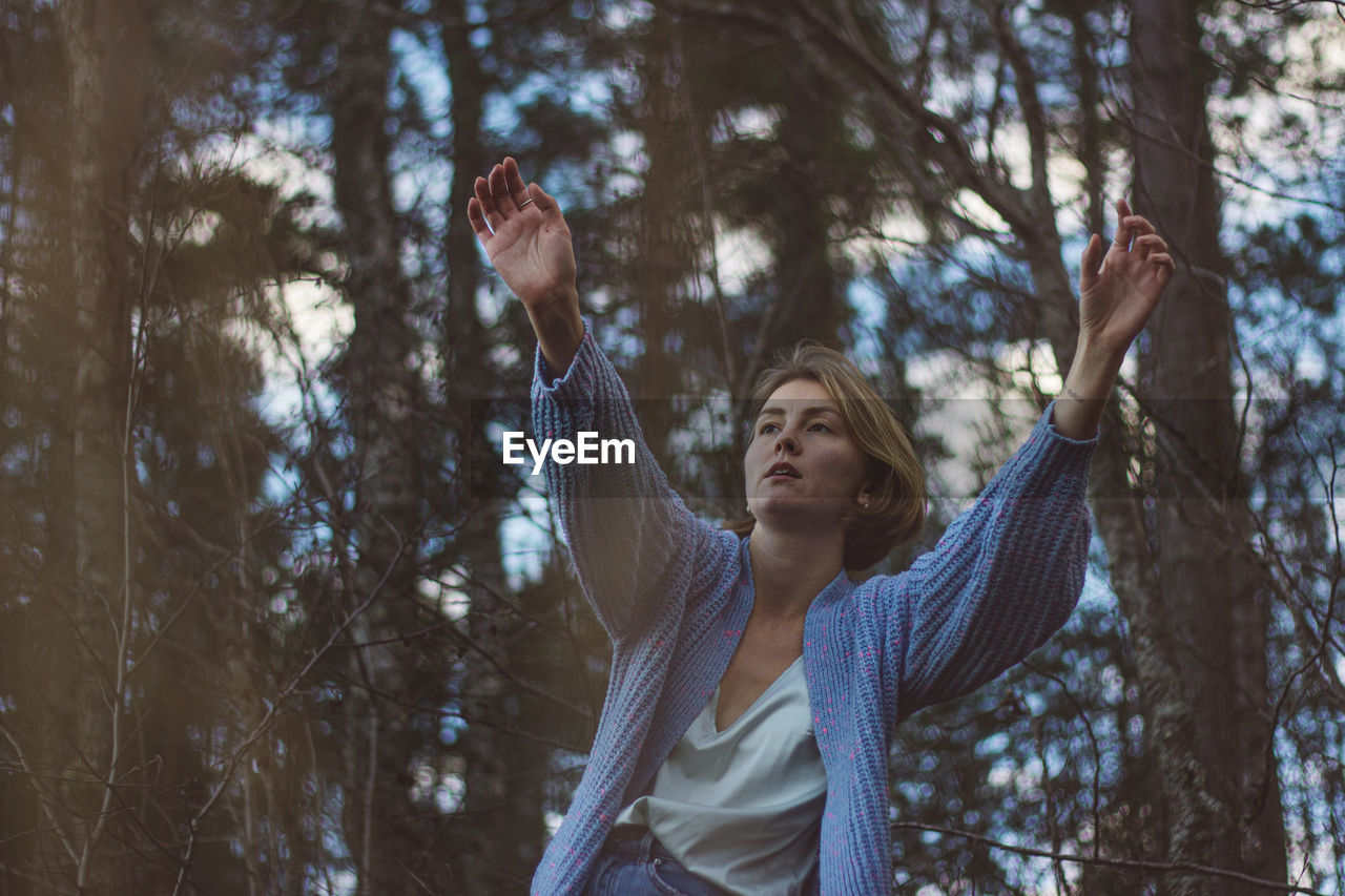 Young woman with short hair dancing against trees in forest