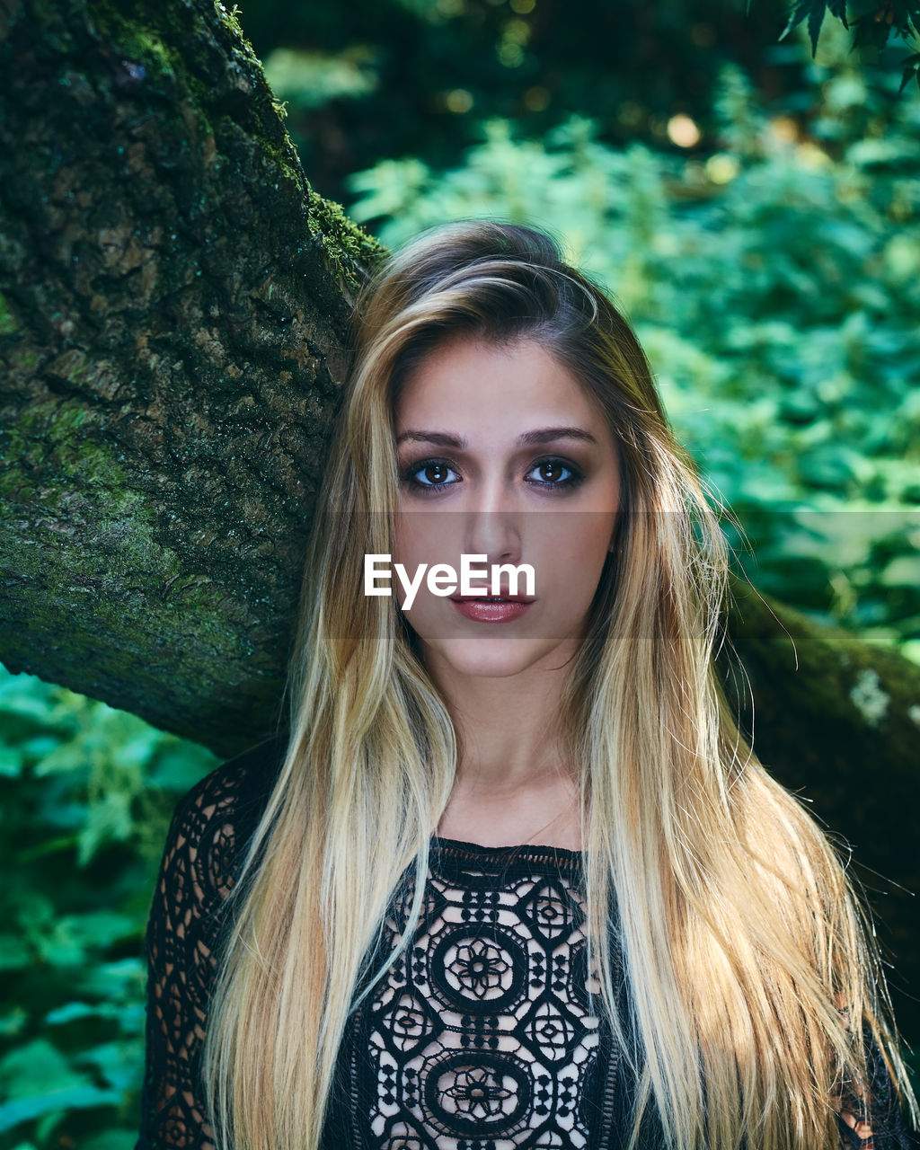 Portrait of young woman standing against tree