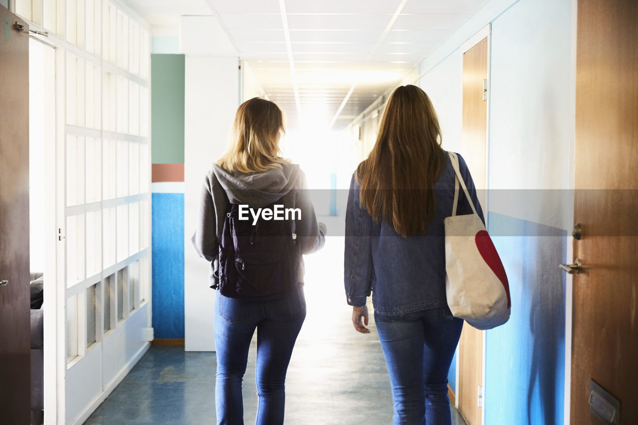 Rear view of friends walking in corridor at university on sunny day