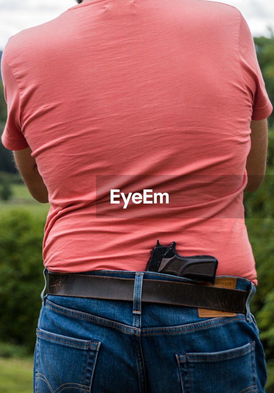 Rear view of man standing outdoors with a gun