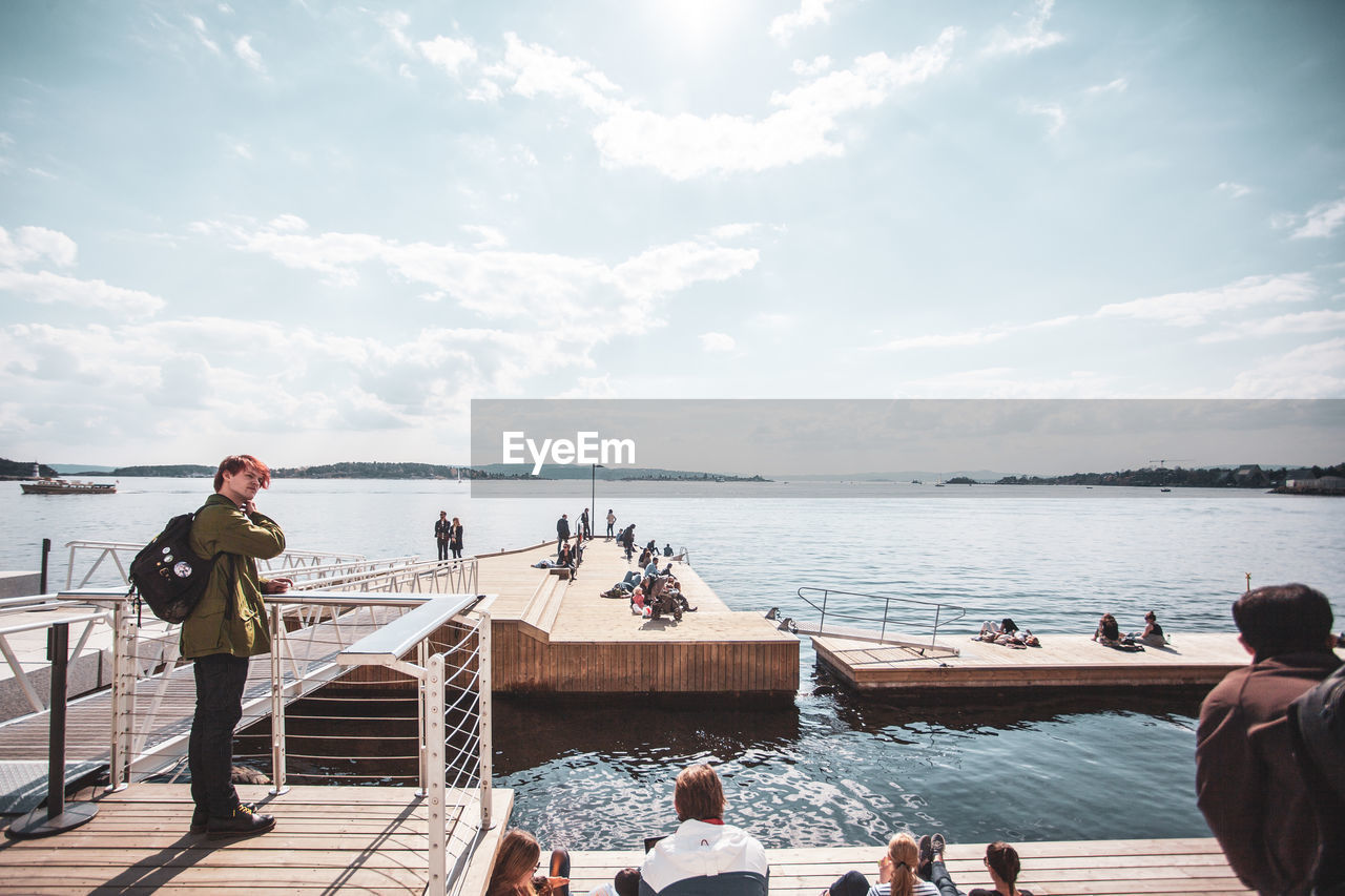 PEOPLE LOOKING AT SEA AGAINST CLOUDY SKY