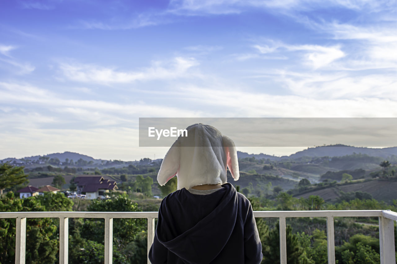 Rear view of boy wearing mask while standing against landscape