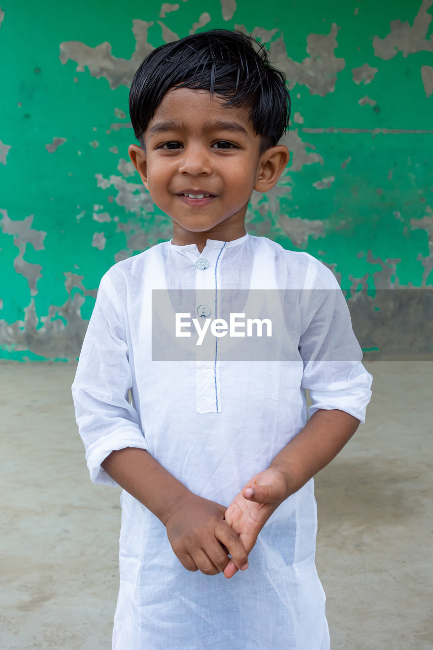 PORTRAIT OF CUTE SMILING BOY STANDING AGAINST WALL