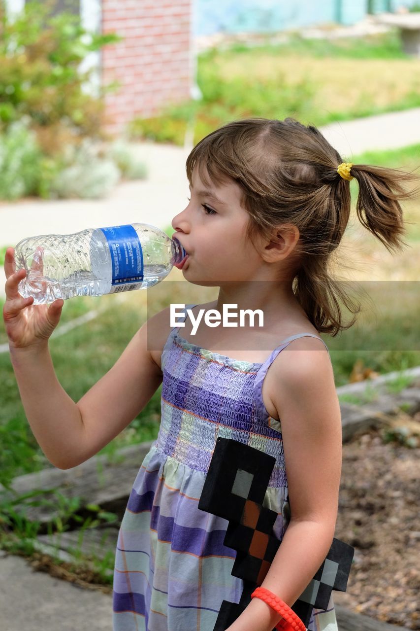 Girl drinking water from bottle while standing at playground