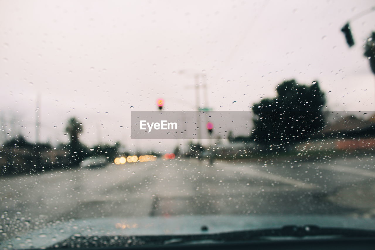 Road against sky seen through wet car windshield during rainy season