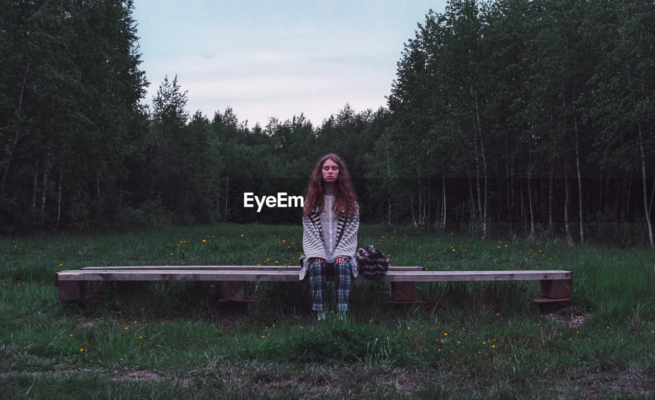 FULL LENGTH PORTRAIT OF WOMAN SITTING IN PARK AGAINST TREES