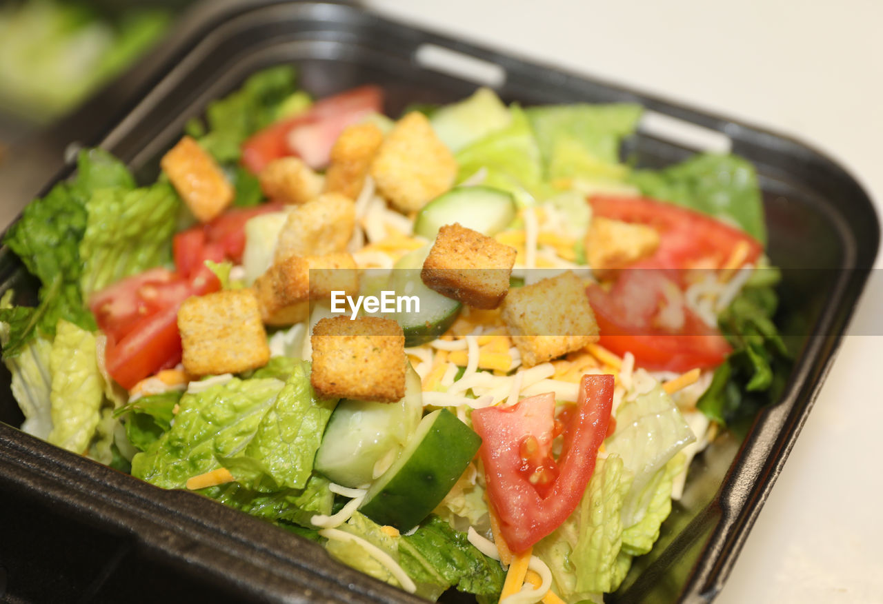 Salad mix of lettuce, tomato and cucumbers topped with cheese and croutons, served in a to-go box.