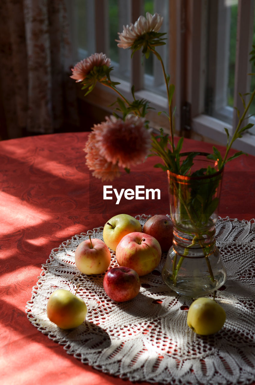 Appples and flowers in vase on table. 