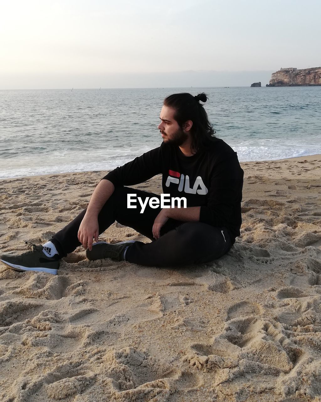 Young man sitting on shore of beach against sky