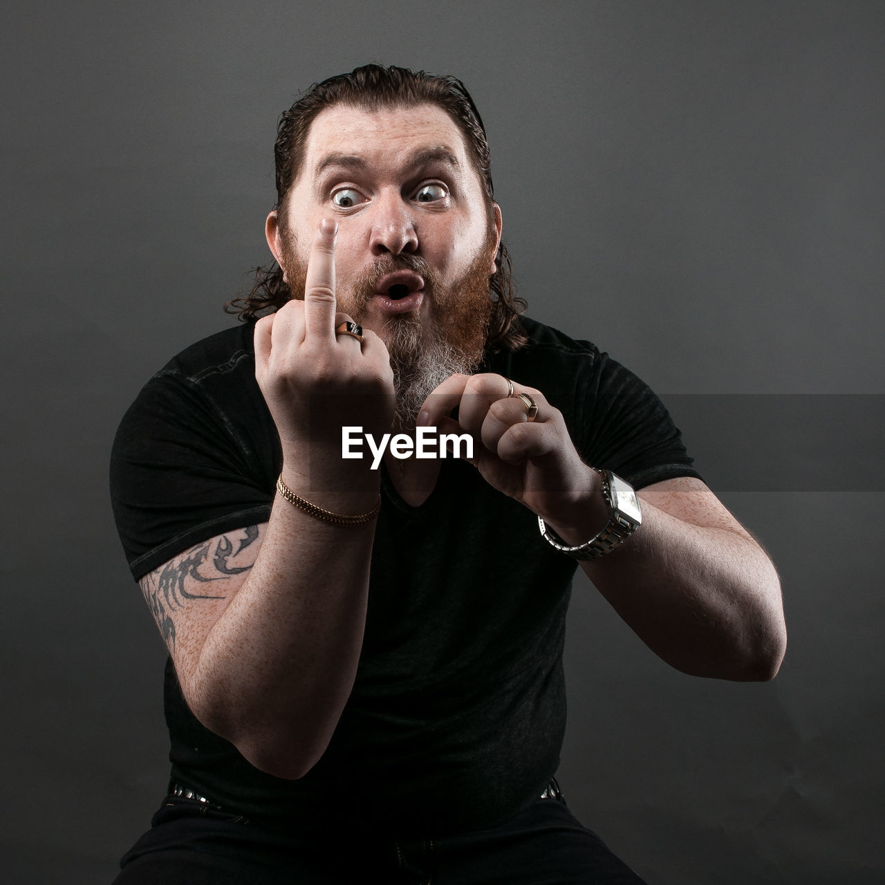 Mid adult man gesturing obscene gesture while sitting against black background