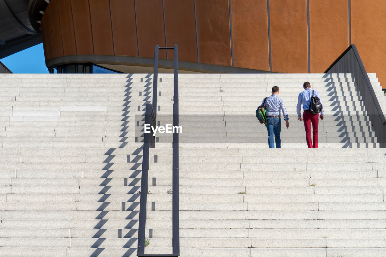 Rear view of men with backpacks climbing staircases