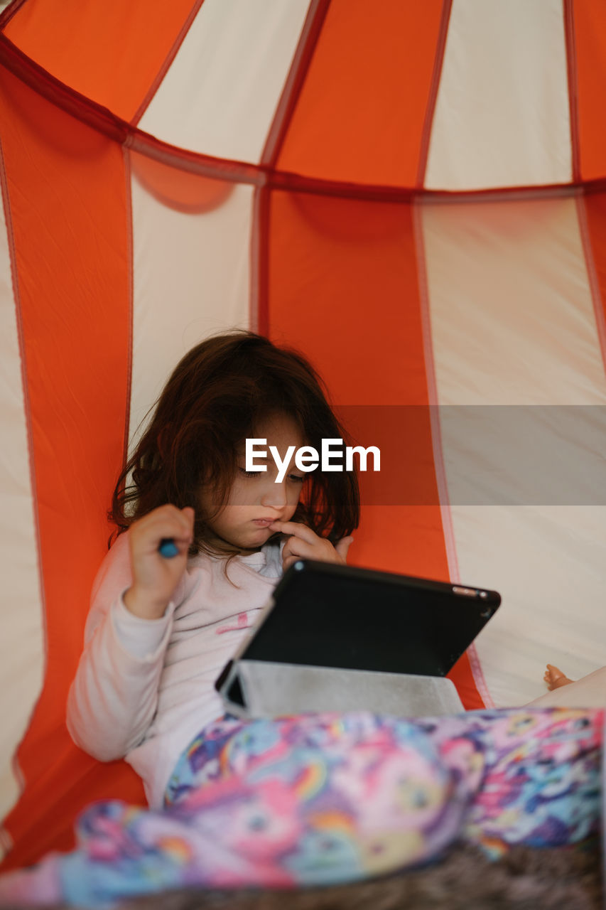 Four-year-old girl in pajamas looking at tablet in a little house