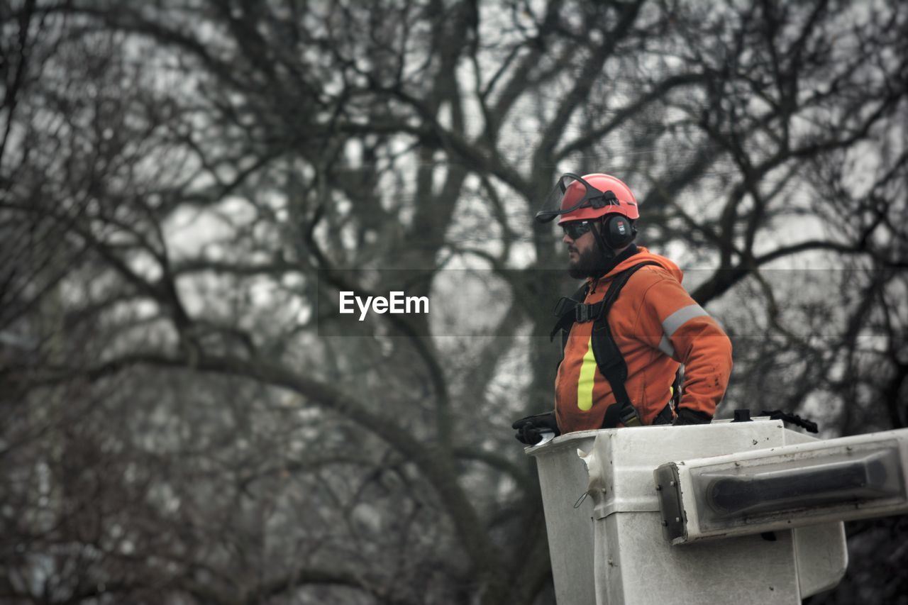 Side view of worker standing in equipment against bare trees