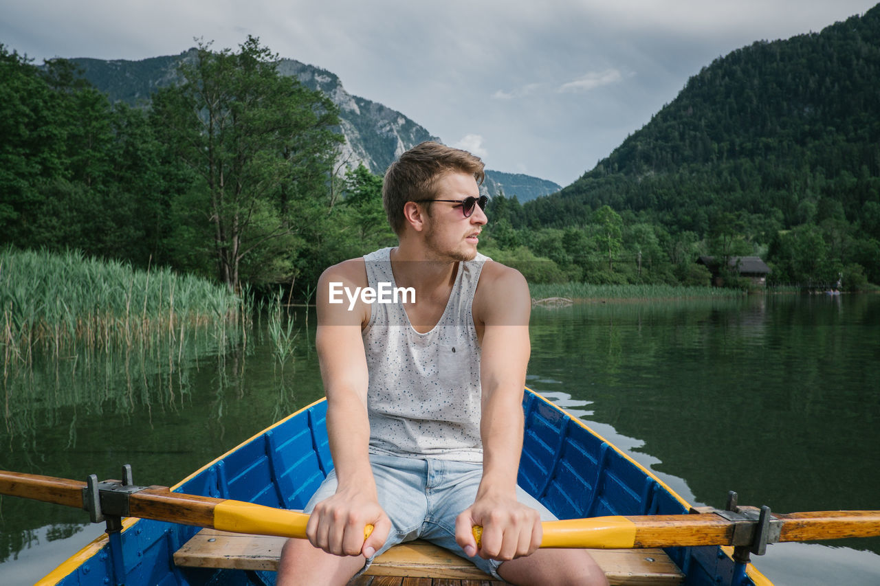 Young man on boat sailing in lake against cloudy sky