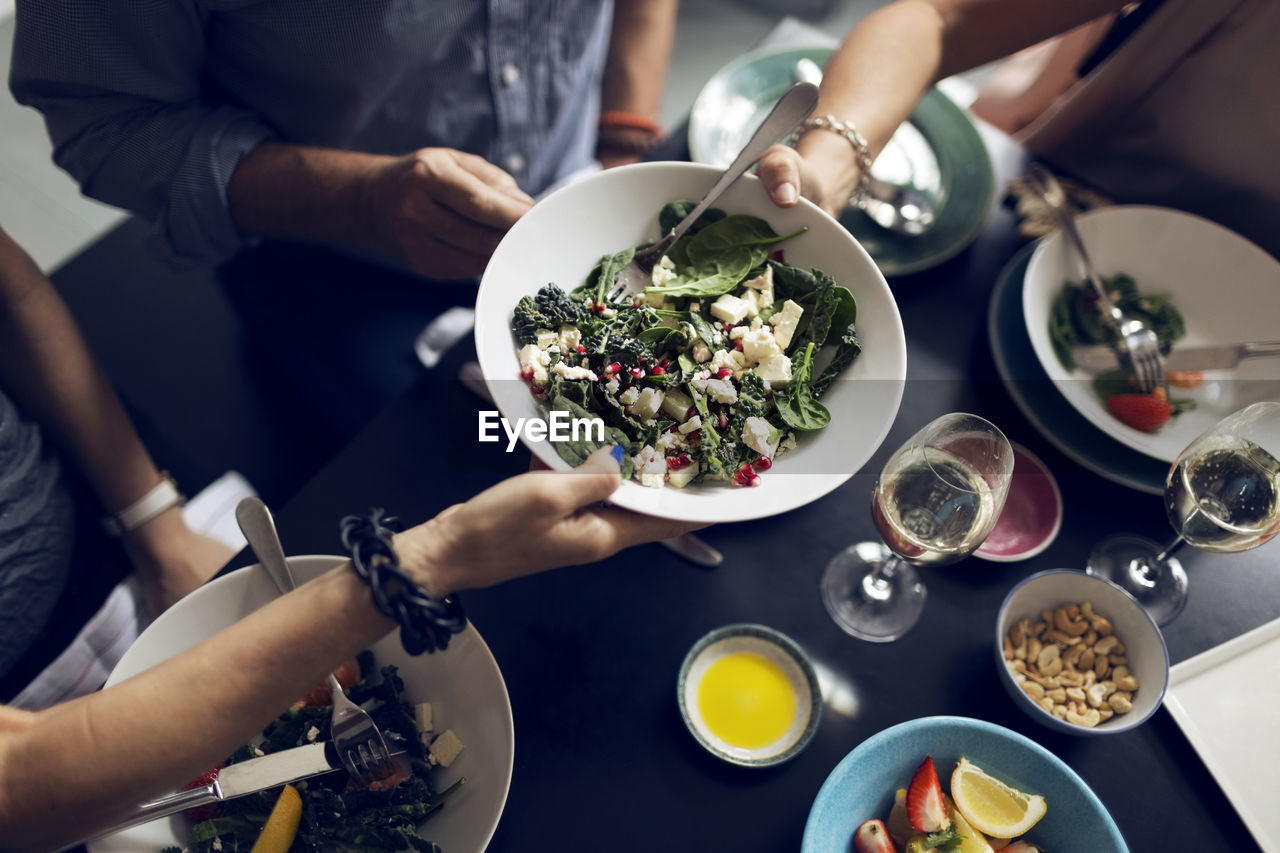 Cropped image of friends holding salad bowl at table