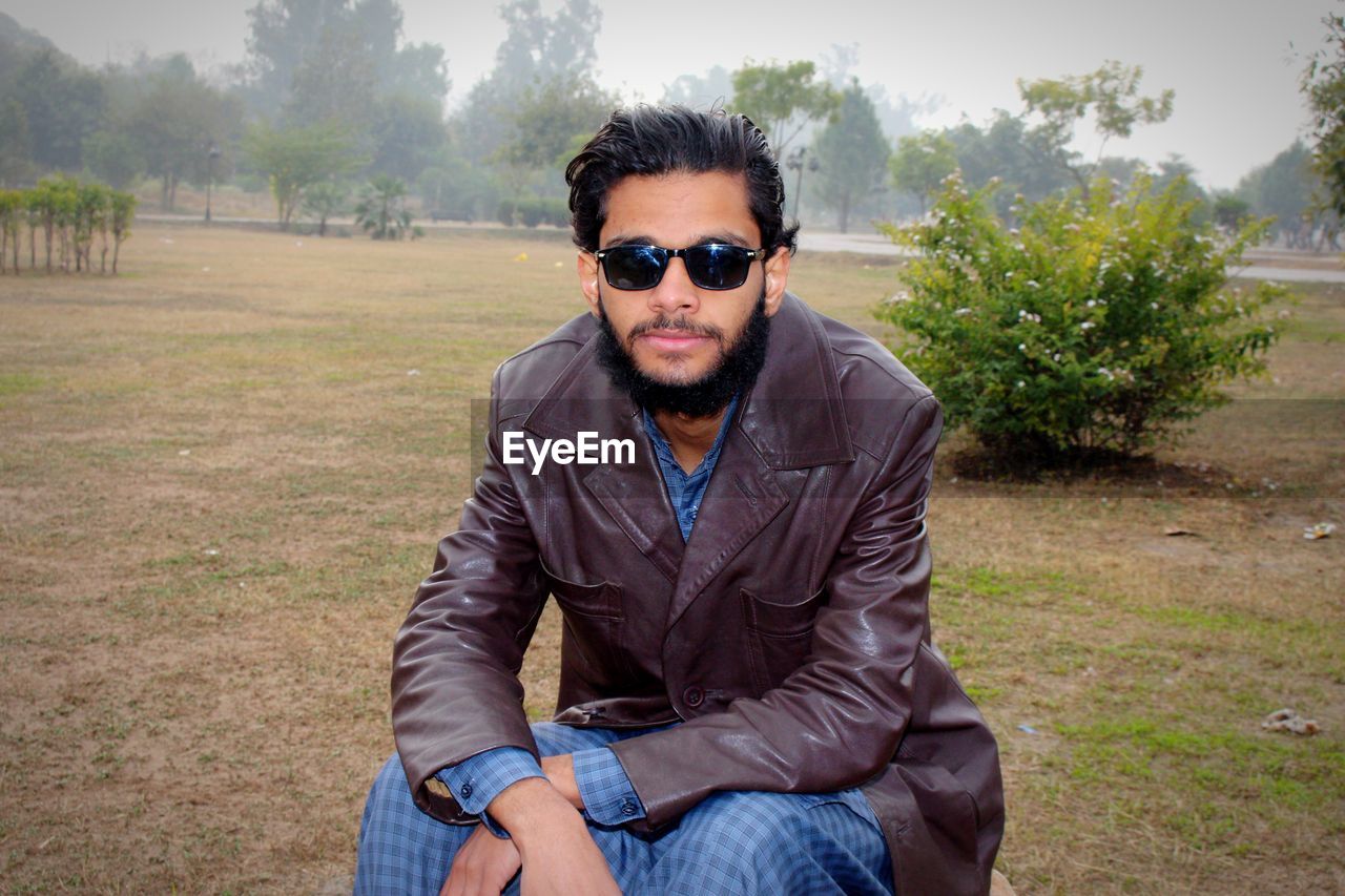 Young man wearing sunglasses while sitting on field