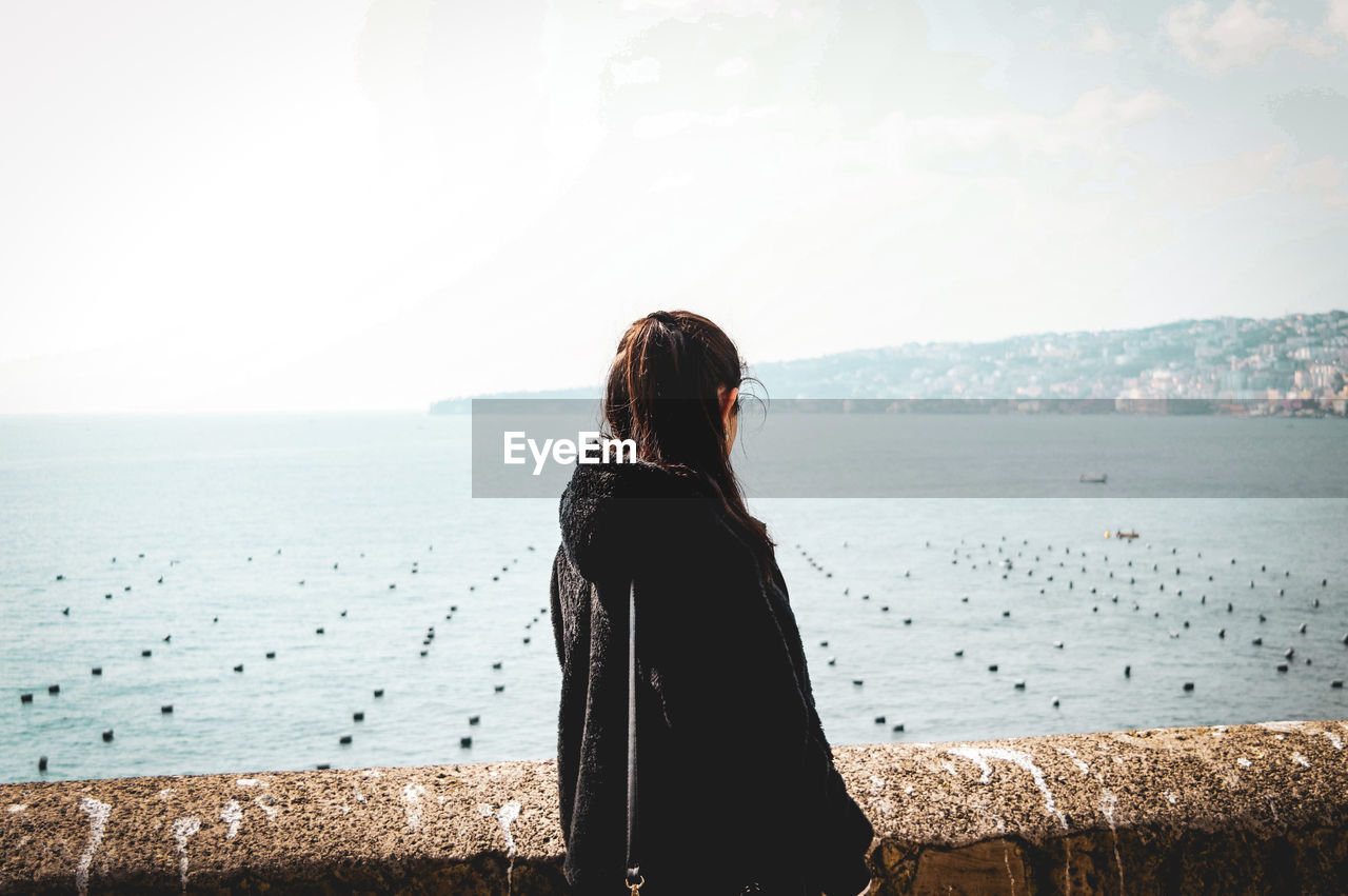 Side view of woman looking at sea while standing on observation point against sky