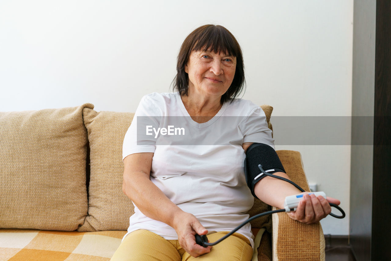 Adult female person measuring her blood pressure and pulse with an electronic