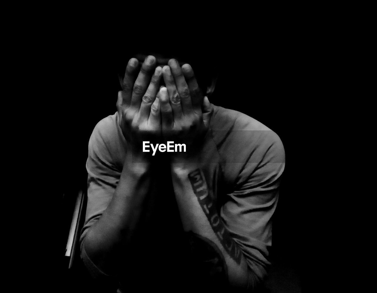 Depressed man covering face against black background