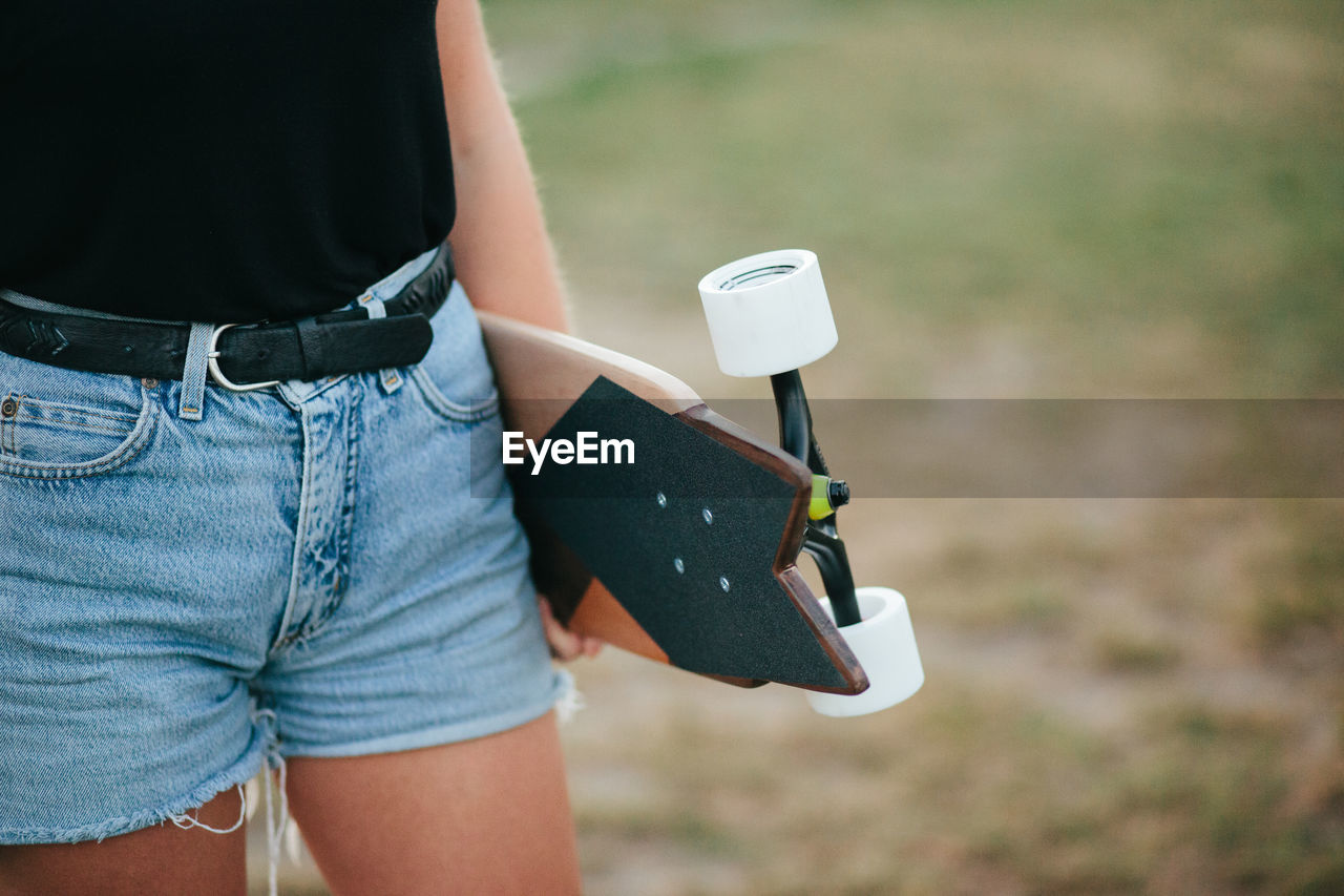 Midsection of woman holding skateboard while standing on field