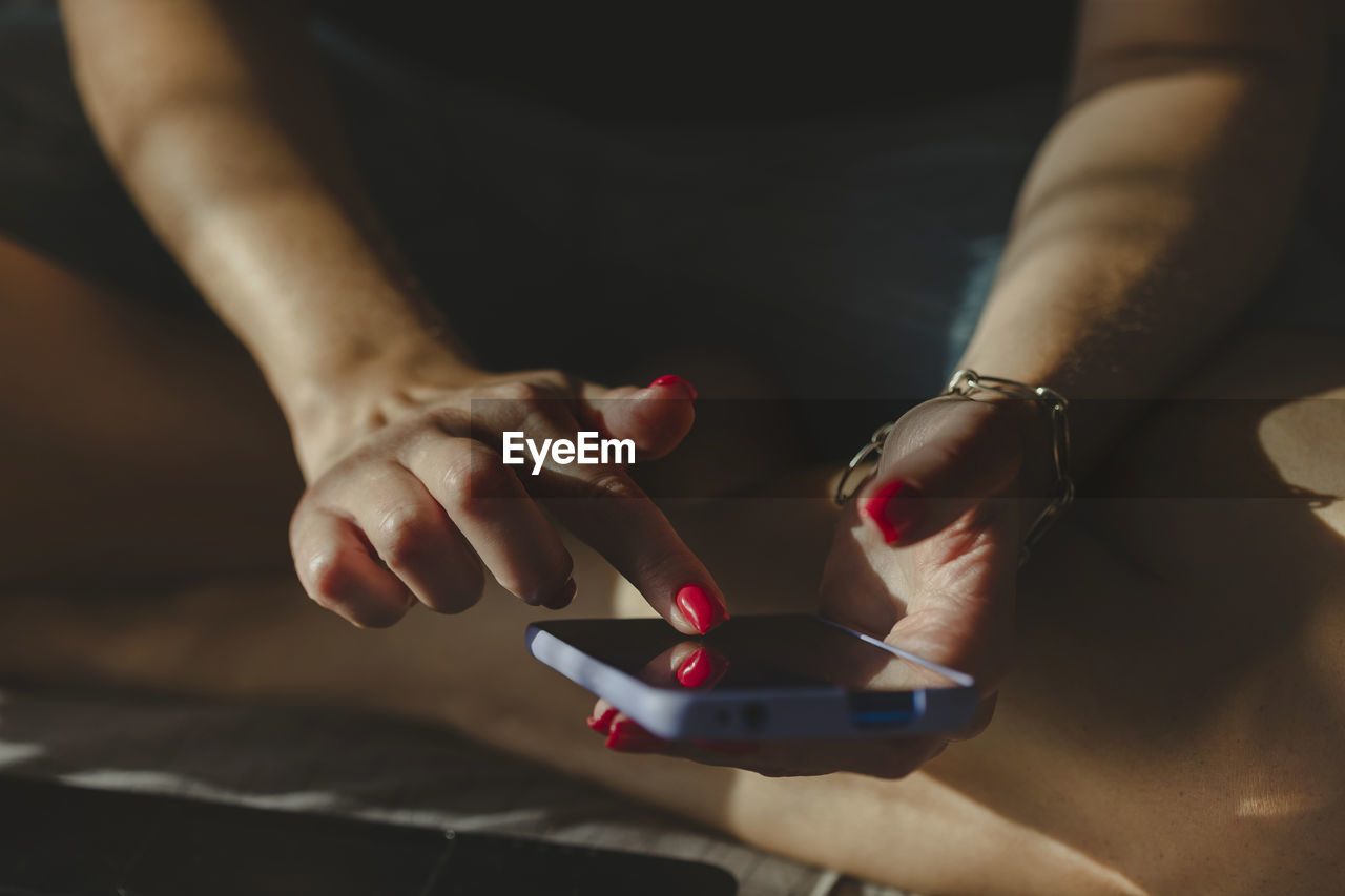 Woman texting using mobile phone, hands with red nail polish manicure in frame. online shopping.