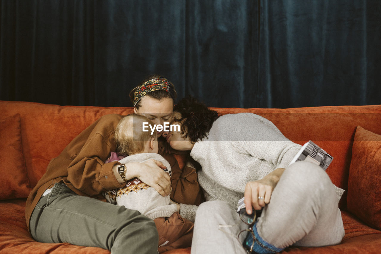 Lesbian mothers with daughter sitting on sofa at home