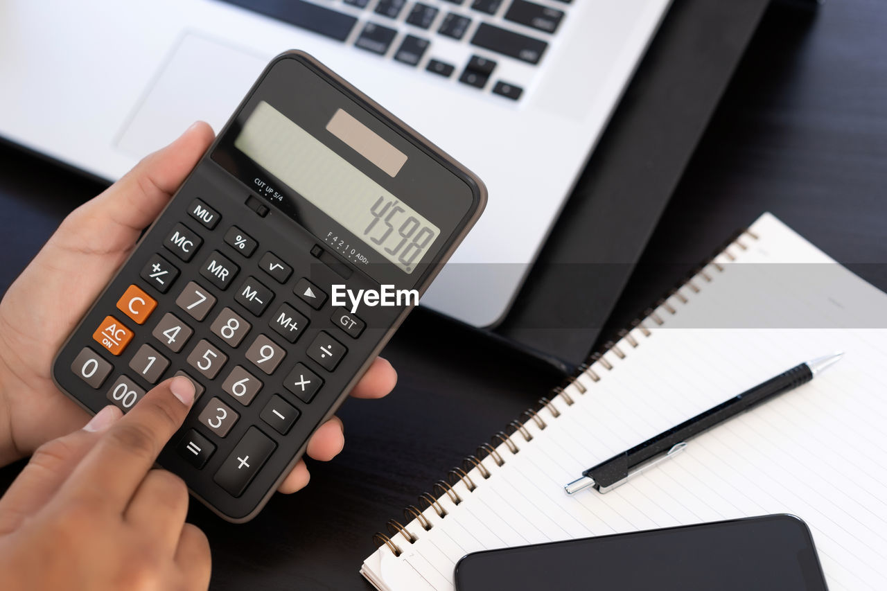 Cropped hands of business person using calculator at desk