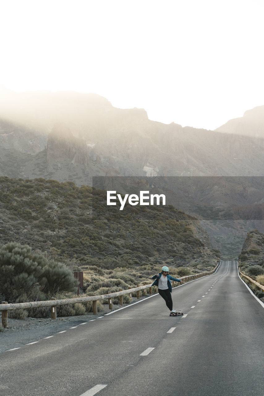 Full length of woman skateboarding on road against mountains