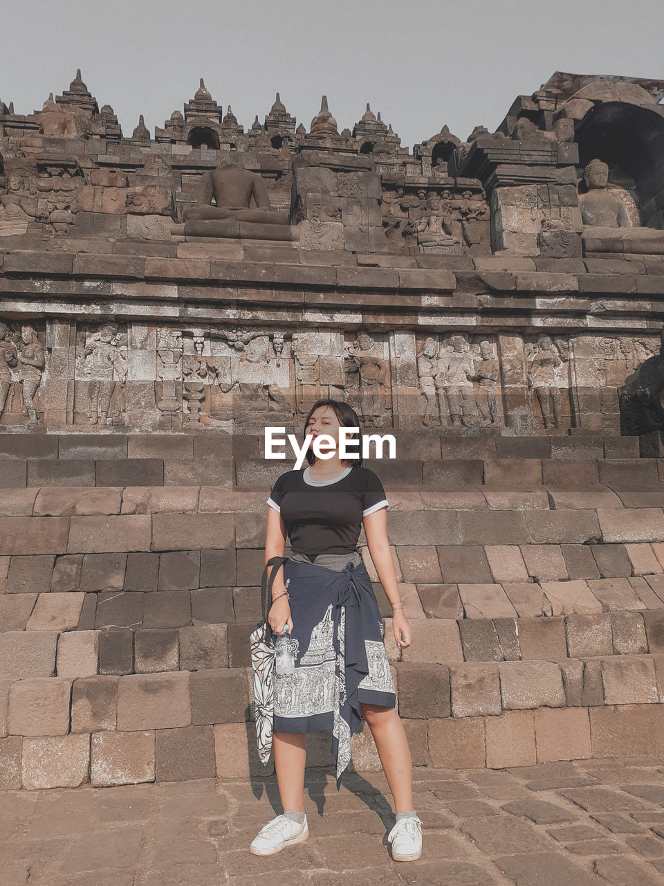 Full length of young woman standing against brick wall