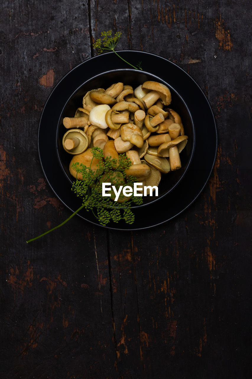 Salted milk mushrooms with green sprigs of dill in a black bowl on a black wooden table