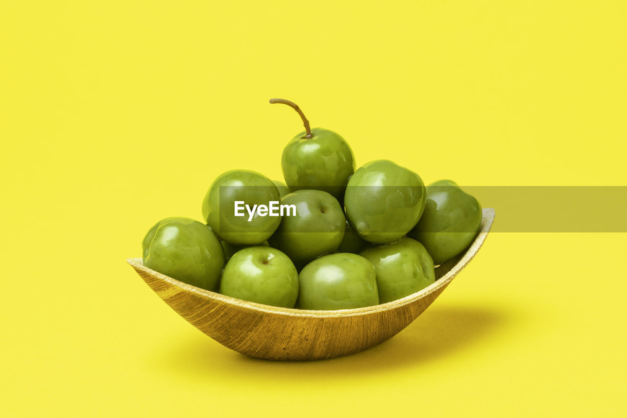 Close-up, a palm leaf bowl full of fresh green olives on a yellow table. organic olives in a bowl.