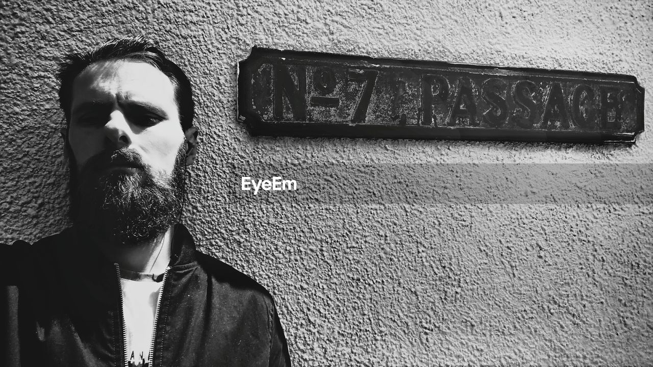 Close-up of bearded man standing by information sign on wall
