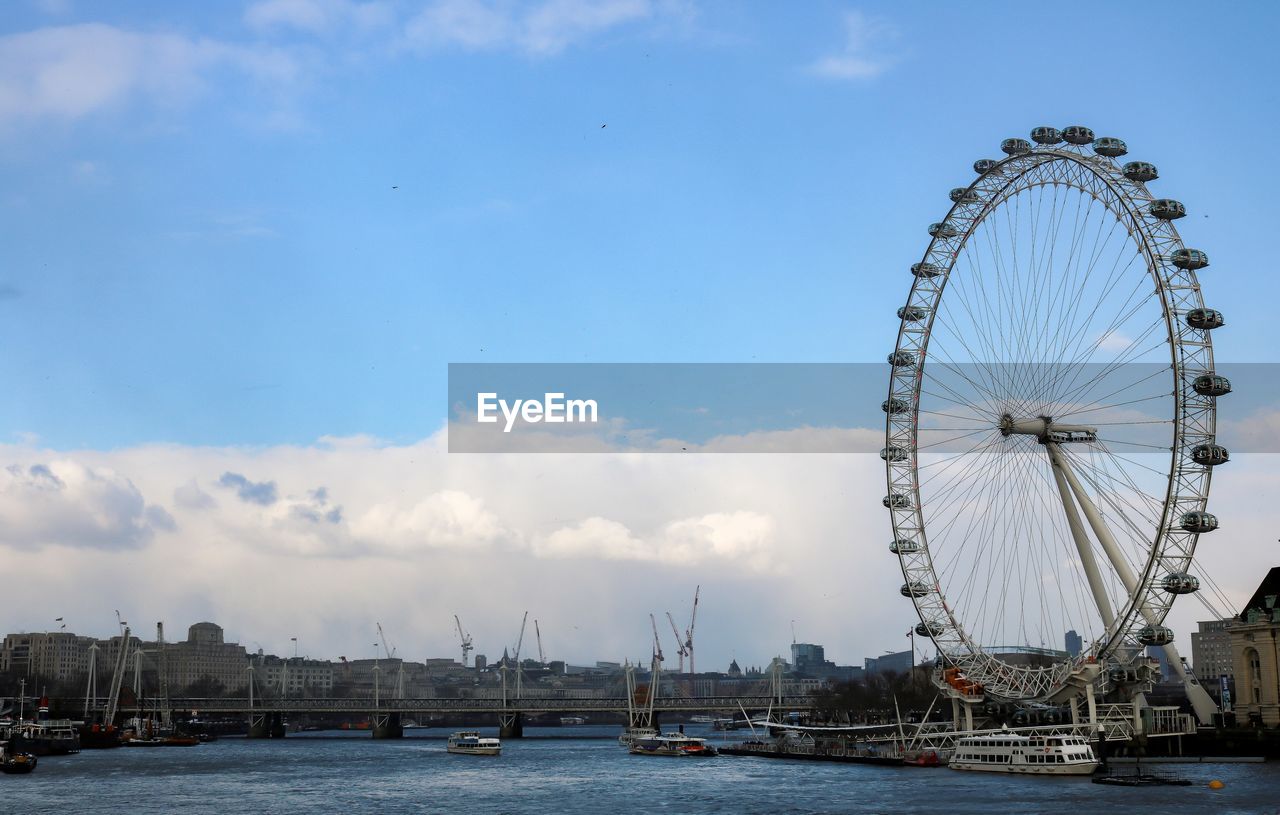 Ferris wheel by river in city against sky