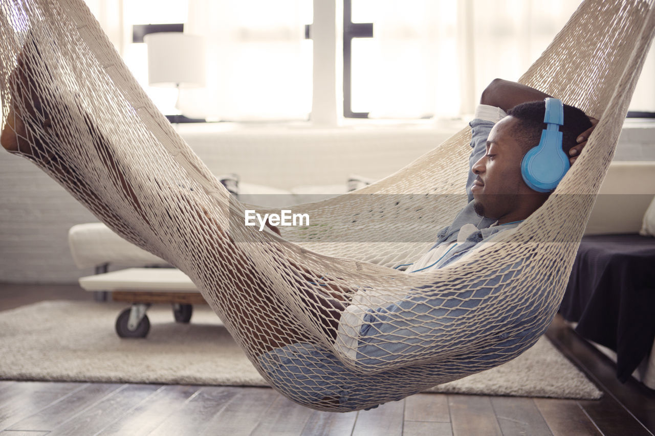 Man listening music while resting on hammock in living room at home