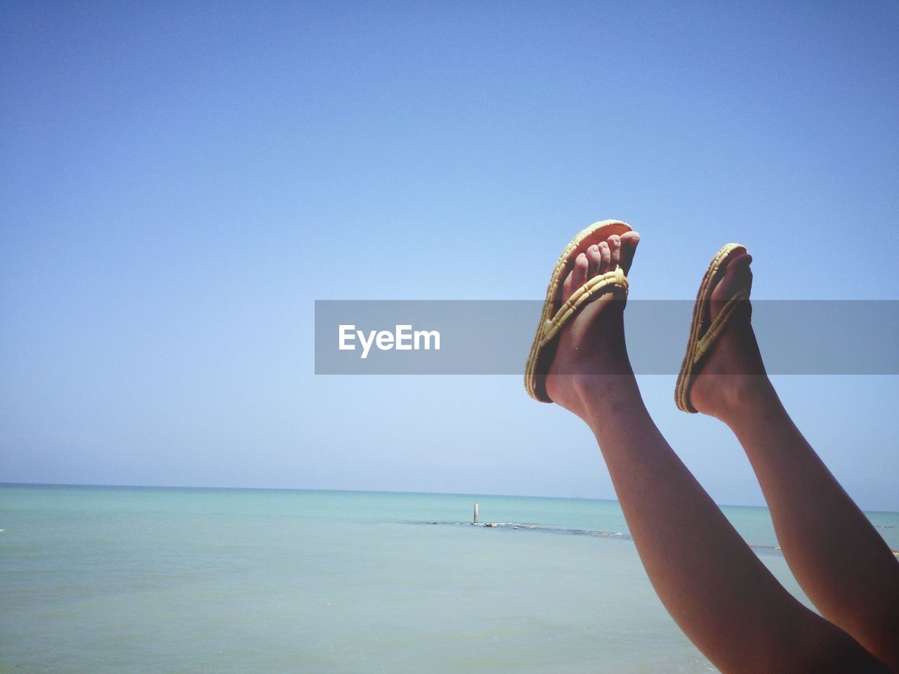 Low section of woman at beach against clear blue sky