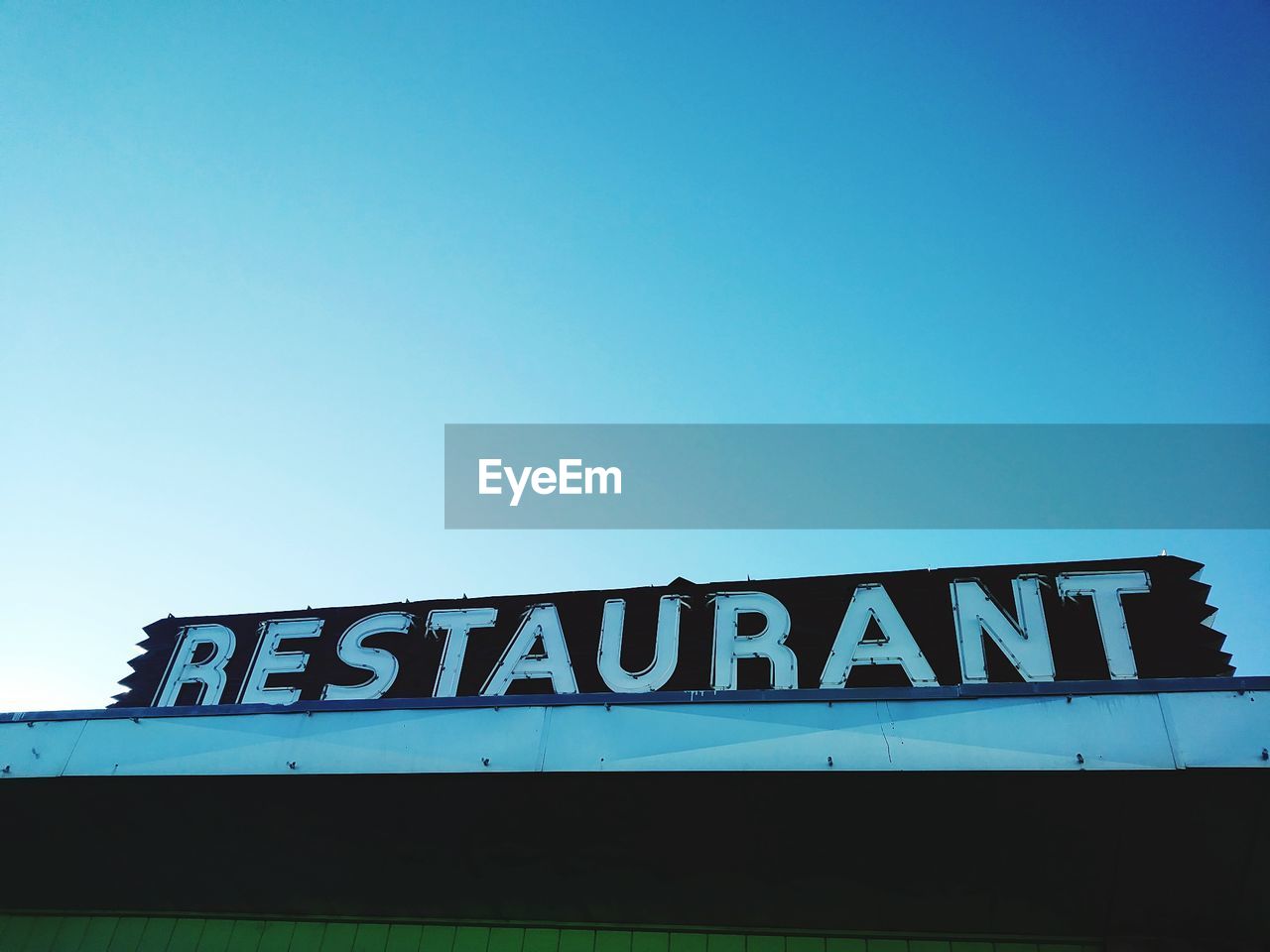 Low angle view of restaurant text against clear blue sky