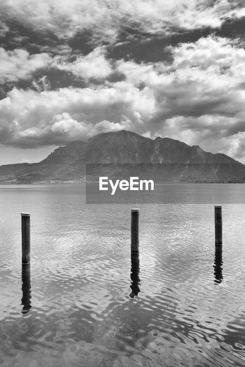 water, black and white, cloud, sky, post, monochrome photography, scenics - nature, wooden post, mountain, monochrome, beauty in nature, nature, sea, tranquility, horizon, tranquil scene, no people, reflection, ocean, day, shore, outdoors, environment, mountain range, wood, landscape, idyllic, white, land, coast, wave, pole, non-urban scene