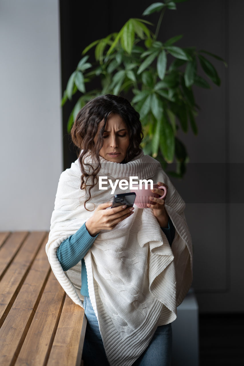 Young unhealthy woman suffering from cold or flu writing sick day email message via smartphone