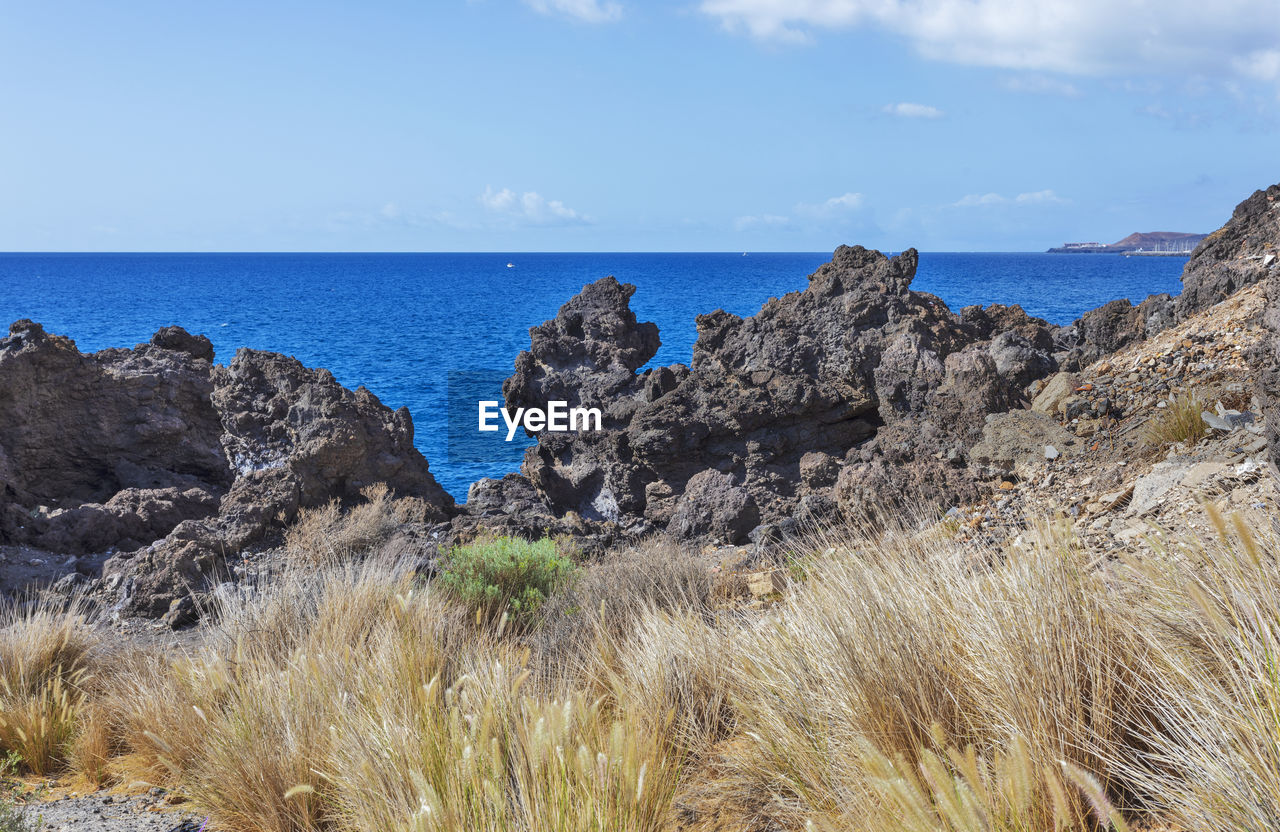 sea, sky, land, water, scenics - nature, rock, nature, beach, beauty in nature, horizon over water, horizon, coast, cliff, shore, landscape, tranquility, plant, tranquil scene, no people, cloud, terrain, travel destinations, day, geology, environment, ocean, rock formation, blue, non-urban scene, travel, grass, outdoors, coastline, tourism, vacation, idyllic, mountain