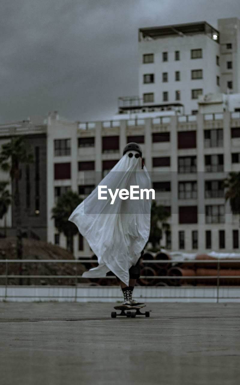 Rear view of skater ghost standing in city in a longboard